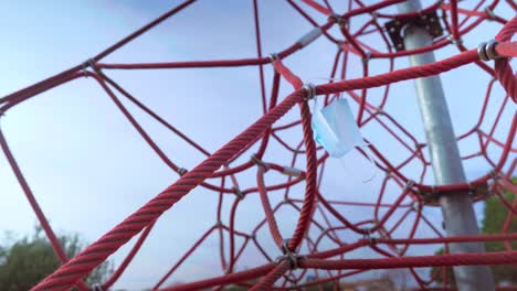 medical protective face mask discarded in a playground rope pyrapid, blown by the wind, pollution during the coronavirus covid-19 pandemic