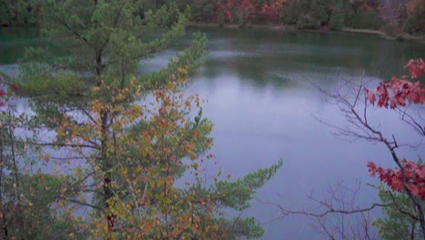 Slow-rising-shot-from-looking-down-over-the-side-of-a-rocky-hill-to-a-lake-in-a-forest-with-fall-colours