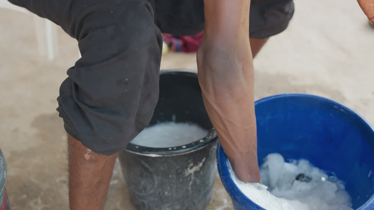 Tarefa doméstica concluída com sucesso. A luz do sol brilha enquanto a toalha seca na varanda após a lavagem. Mãos enxaguam cuidadosamente uma toalha branca em um recipiente azul enquanto a luz do sol ilumina a espuma e a água