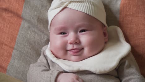 adorable infant baby girl face close-up lying on cushions and smiling showing her tongue