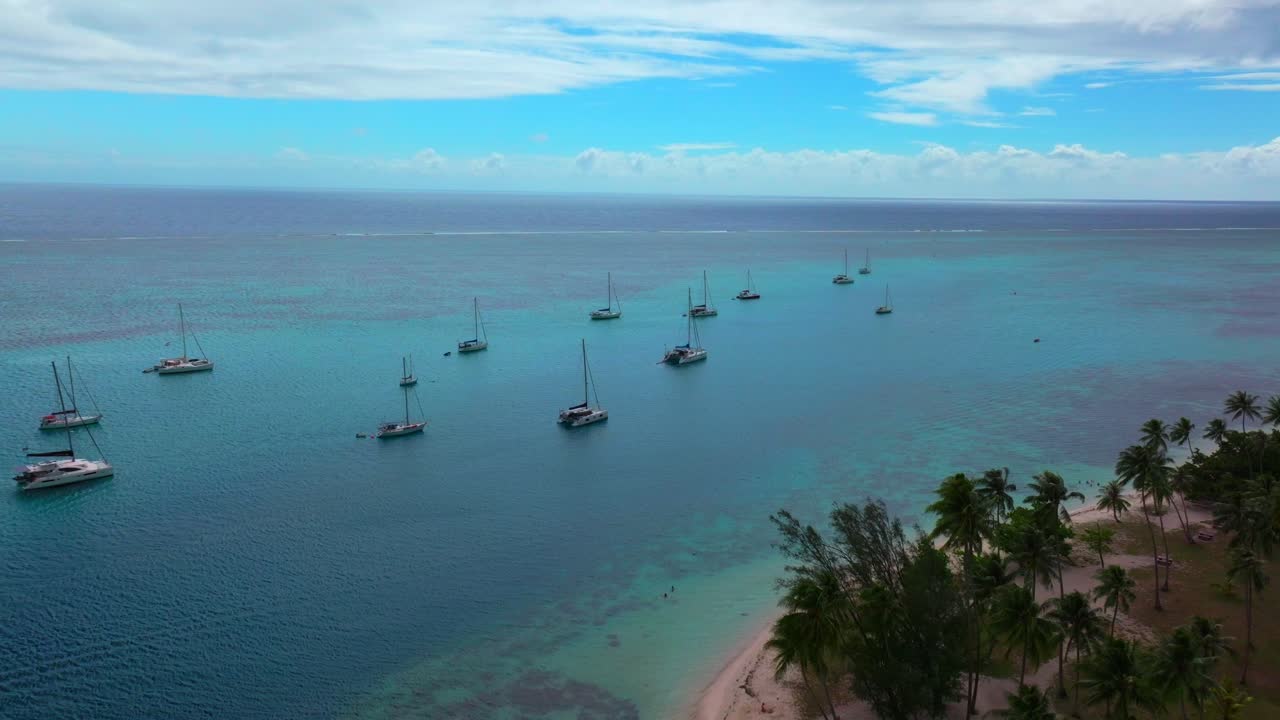 Luftfoto af Moorea, Fransk Polynesien, med sejlbåde forankret ud for Ta'ahiamanu Strand og en rolig lagune, der strækker sig forbi den palmeklædte kystlinje ud i åbent blåt vand.