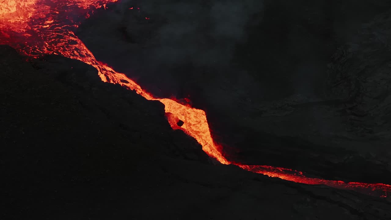 Fresh lava overflowing the volcanic cone, running down into the valley. Drone close up