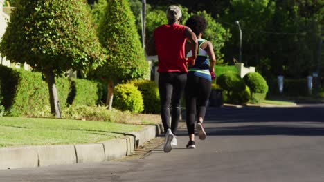 African-american-senior-couple-exercising-outdoors-running-in-sunny-green-road