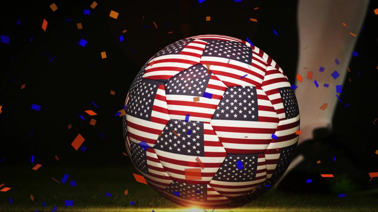 Giocatore che si avvicina, calcia con il tacchetto un pallone da calcio con la bandiera USA, mandando la palla a rotolare a destra, festeggiando.