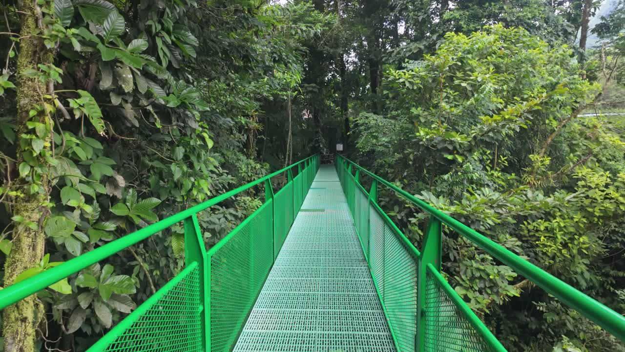 A pedestrian bridge leading to Fortuna Waterfall through a dense tropical forest in Costa Rica