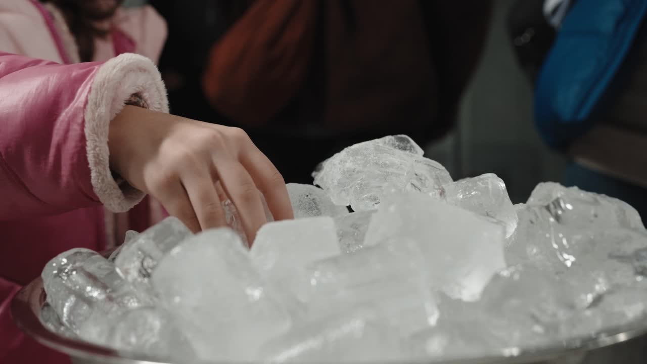 Primo piano di una mano che prende cubetti di ghiaccio da una ciotola di metallo al chiuso