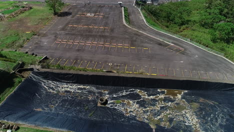 Video-Aéreo-De-La-Planta-De-Tratamiento-De-Aguas-Residuales,-Estanque-De-Retención-Residencial-Al-Lado-De-Un-Gran-Estacionamiento