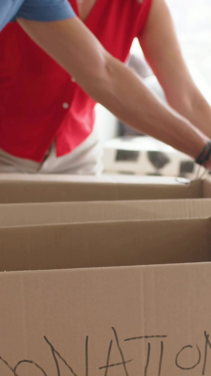 Vertical video: Opening DONAT boxes, couple in blue and red top folding pink shirt at home