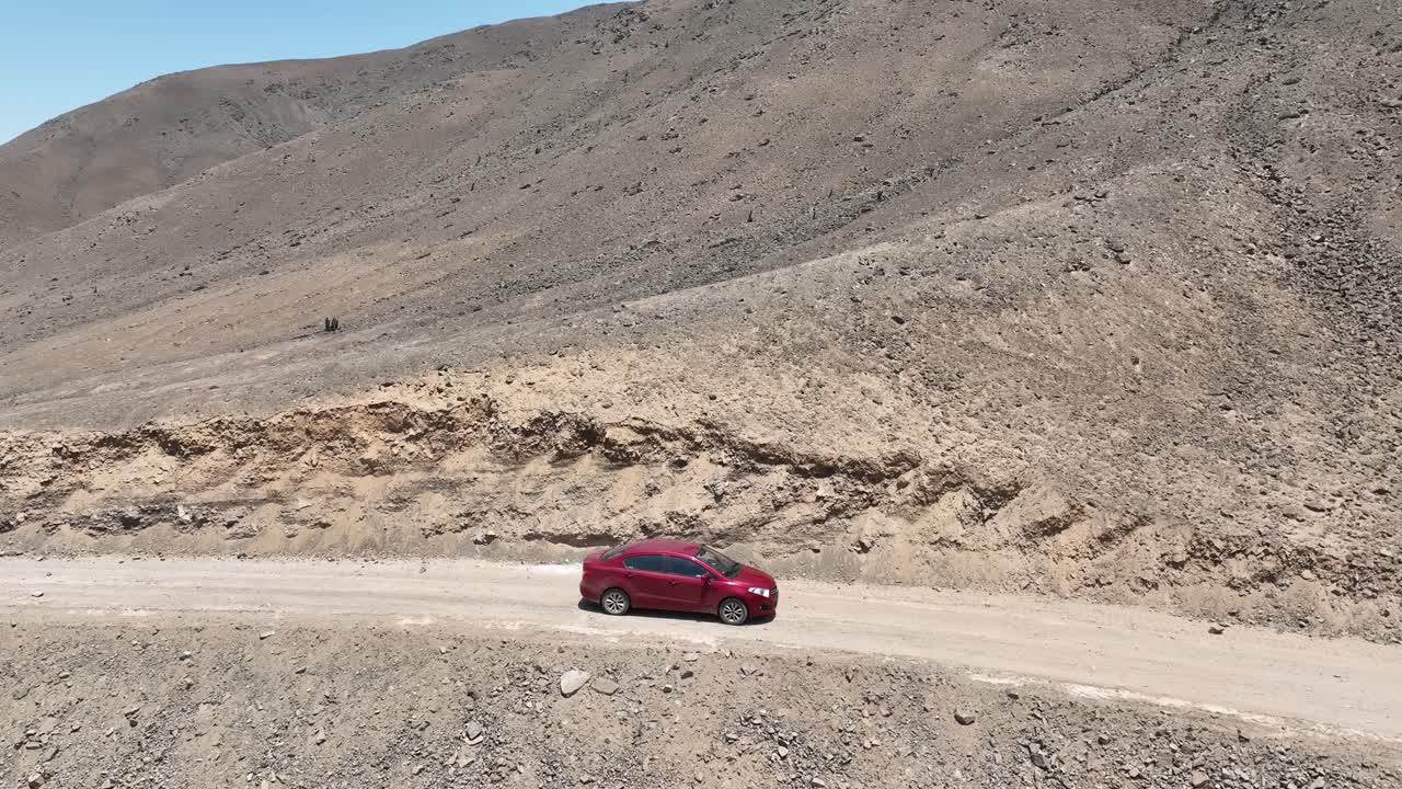 toma panorámica aérea de un camión rojo en movimiento en el páramo de perú en un polvoriento camino seco del desierto a lo largo de las colinas hacia la ciudad santa de caral