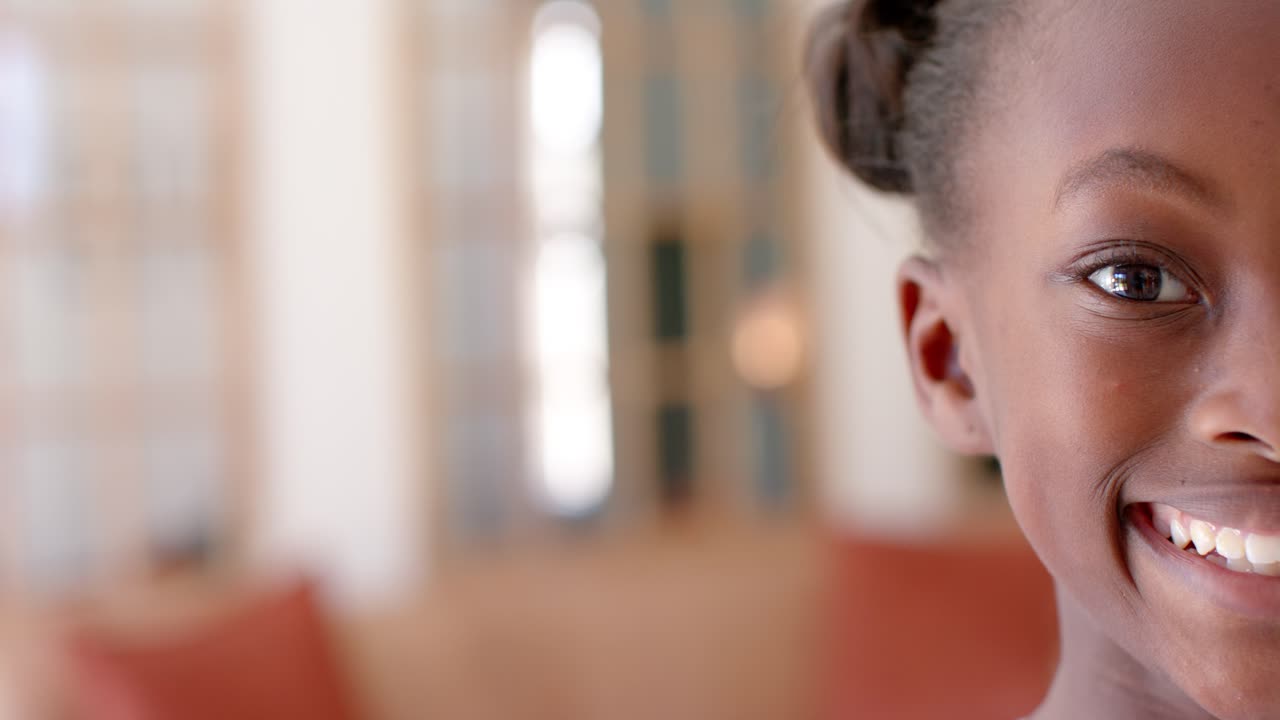 African American girl smiling while responding to camera near window at living-room, copy space