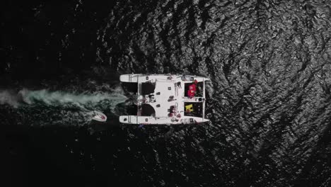 Overhead-shot-of-a-catamaran-full-of-tourists,-sailing-on-the-sea