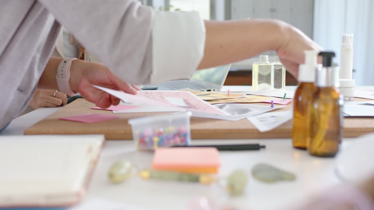 Hands are reaching for papers as project is starting on table, arranging sticky notes and bottles