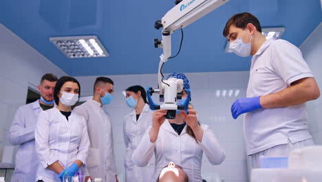 female dentistry student setting the microscope above the patient. teacher stands beside giving recommendations. group of students at backdrop.