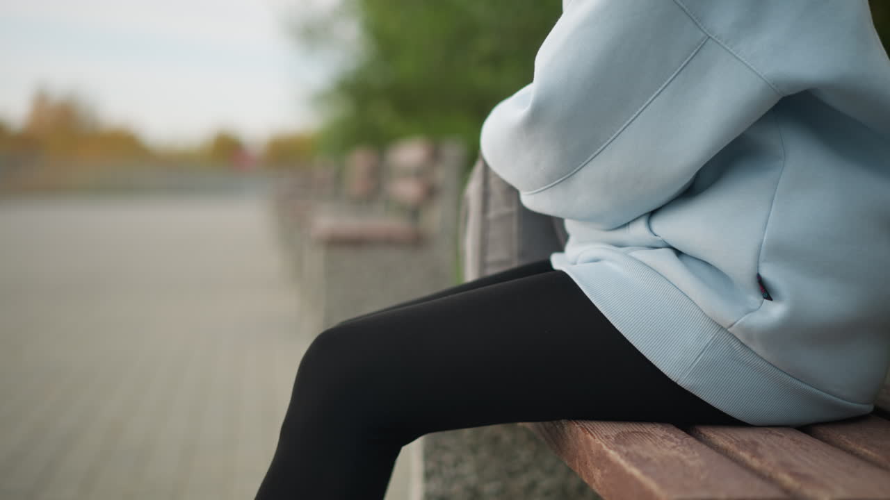 Aerial view of lady holding water bottle, opening it while sitting on bench in park, background blurred, focused on hydration and relaxation, perfect for wellness and nature moments