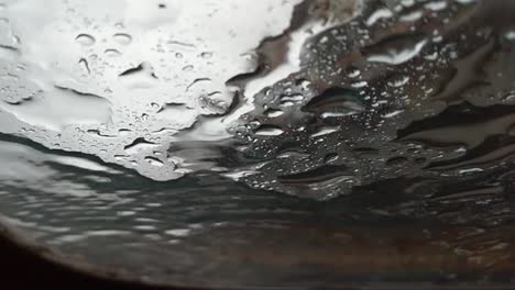 vista abstracta en cámara lenta de las gotas de lluvia aterrizando en el vidrio como se ve desde abajo, debajo, cielo gris