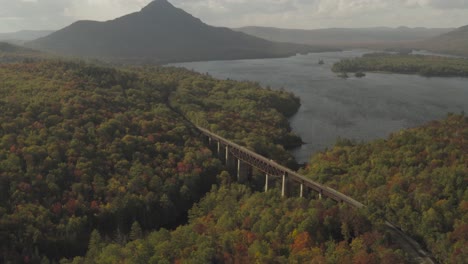 A-mountain-and-railroad-trestle-on-the-shore-of-a-wind-blown-lake-during-early-fall-golden-hour-AERIAL