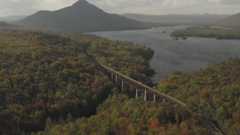 a mountain and railroad trestle on the shore of a wind blown lake during early fall golden hour aerial