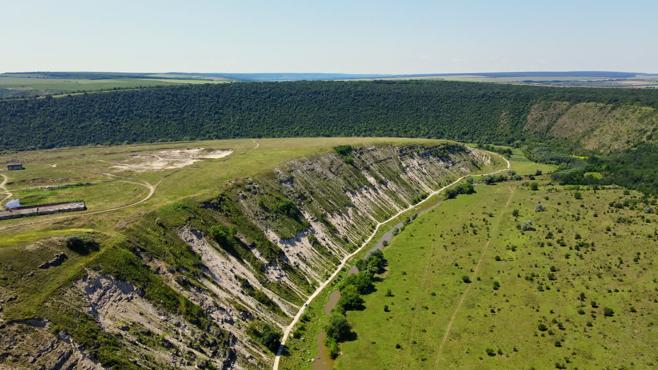 Aerial drone view of a valley with floating river, hill slopes, greenery, fields and village in Moldova