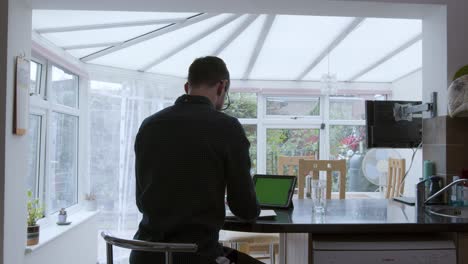 Smartly dressed man using a green screen tablet device and writing on a notepad from home wide shot