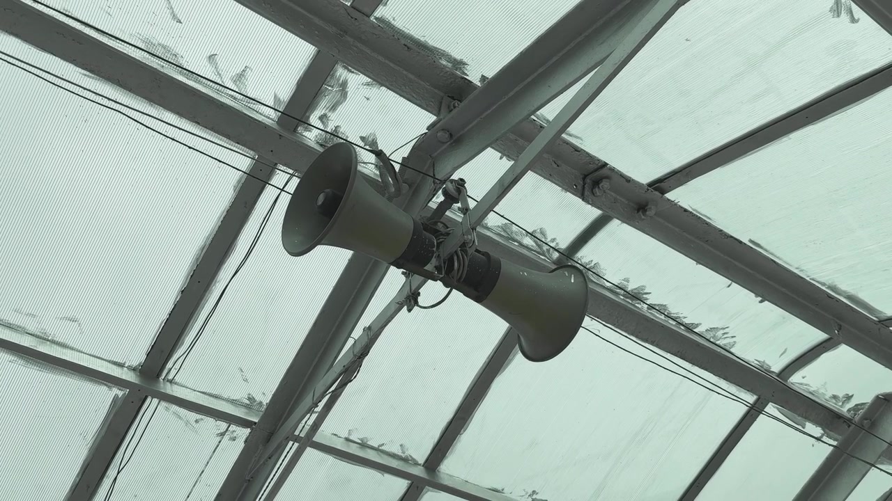 Orbiting close up of a public address loudspeaker mounted beneath a steel roof structure in a transport facility