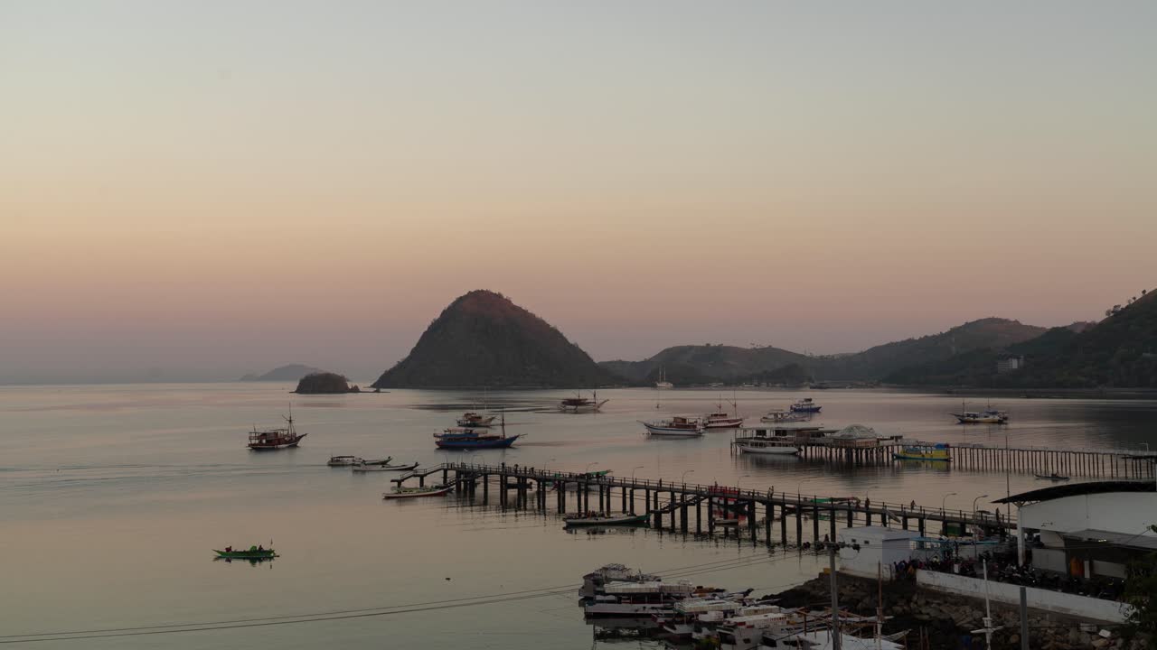 Sunset over a bustling harbor with boats and a pier in a tropical bay