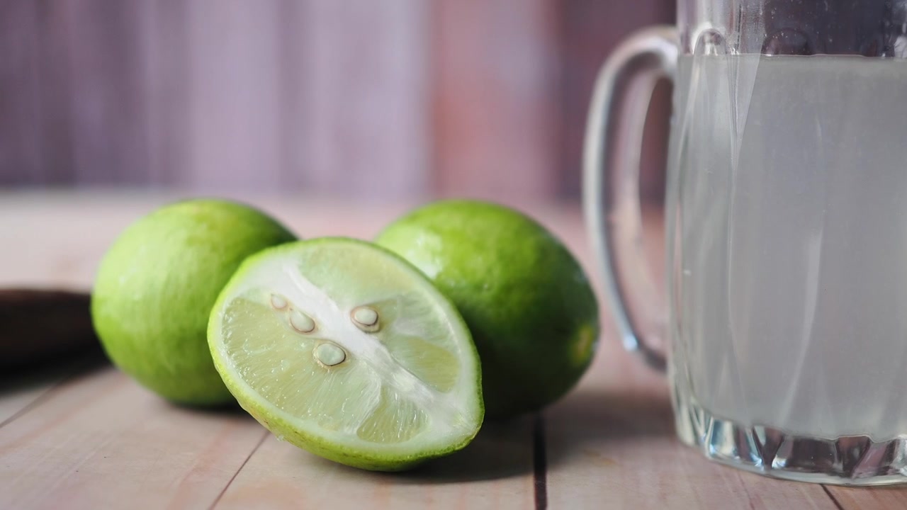 Friske limefrugter og et glas limesaft på et træbord