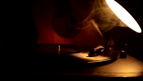 slider shot. vintage vinyl record playing on player and acoustic guitar on background with fire orange smoke. crime or blues concept with toy car installation. selective focus