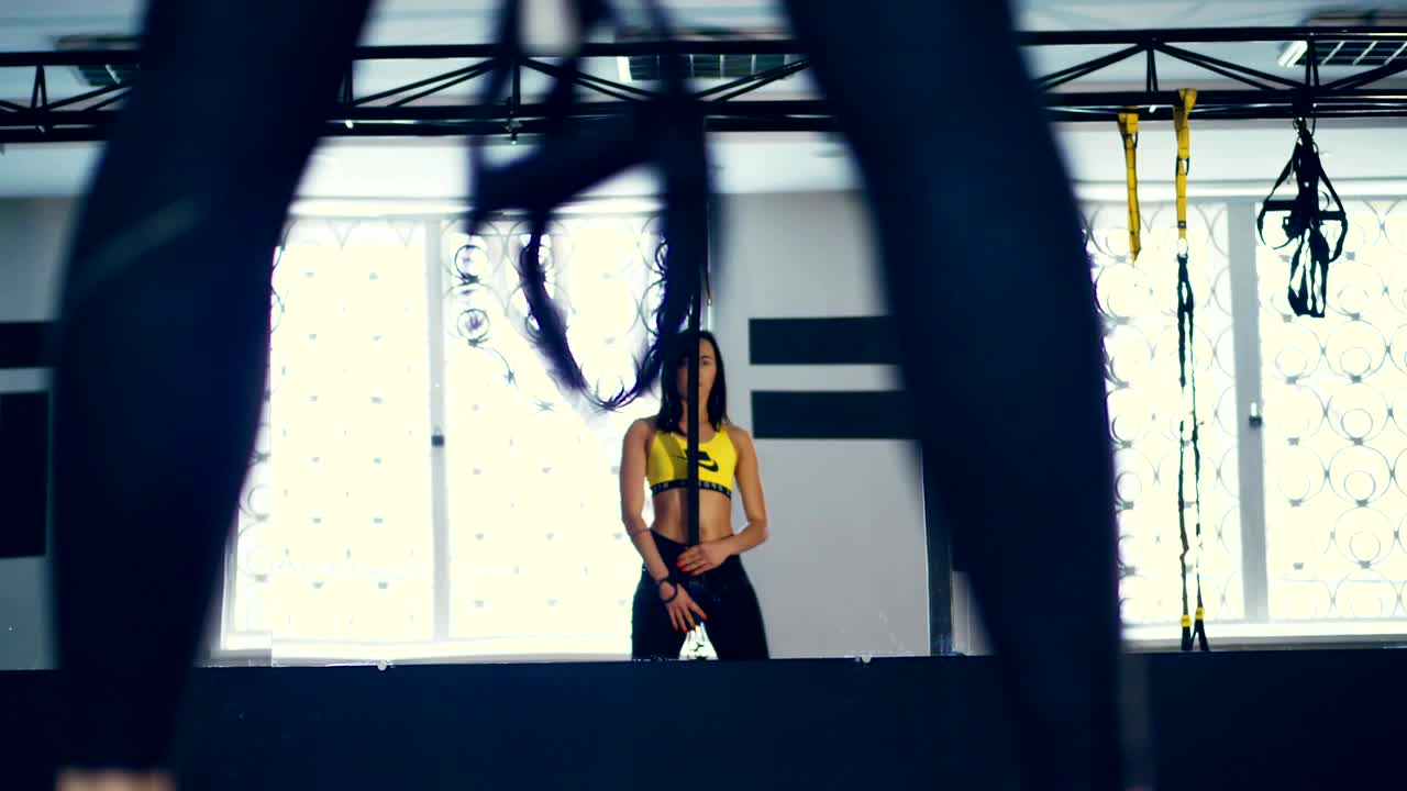 mujer morena bonita con un cuerpo atractivo, mirándose seductoramente en el espejo, sostiene bucles, correas en sus manos, prepara equipos para el entrenamiento. mujer atractiva va para los deportes