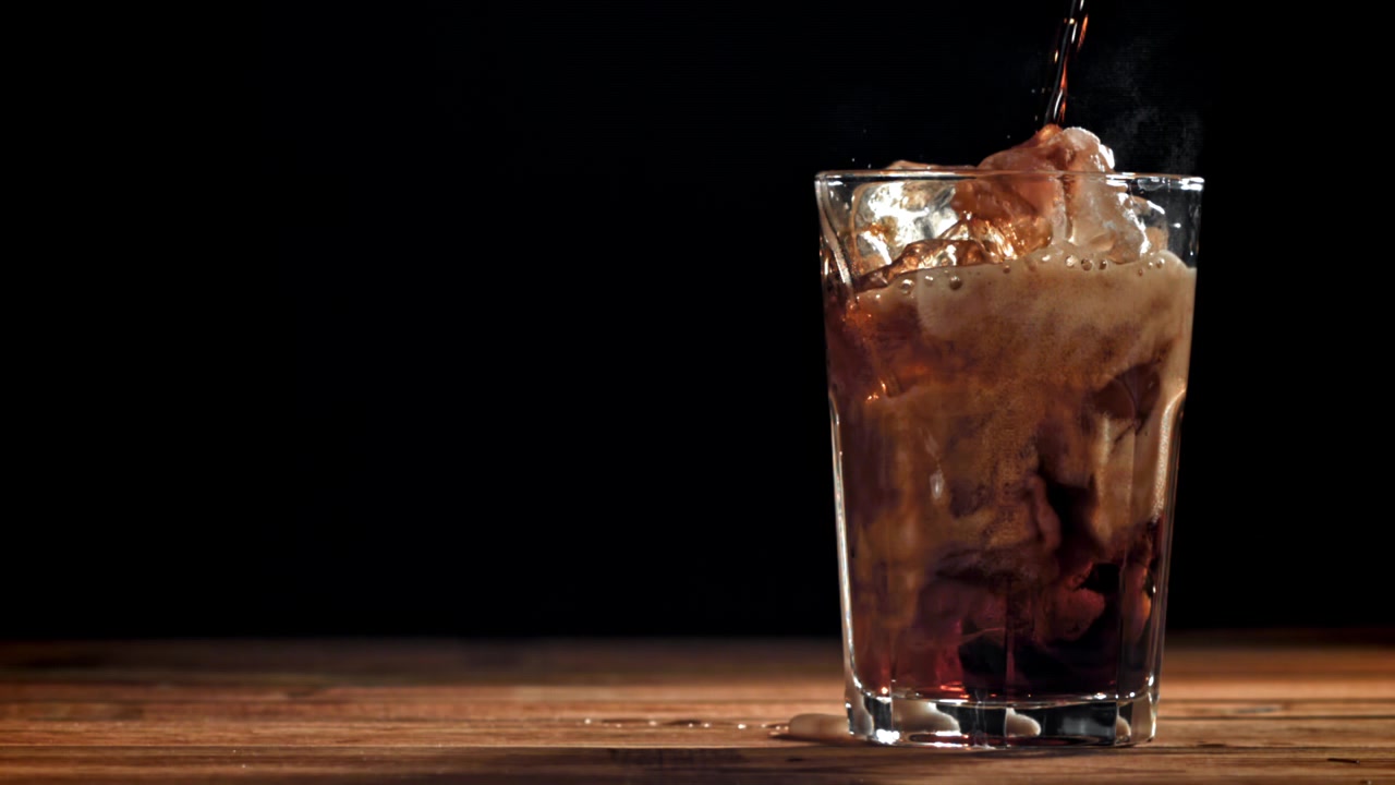 Bevanda rinfrescante alla cola versata in un bicchiere con ghiaccio e uno schizzo.