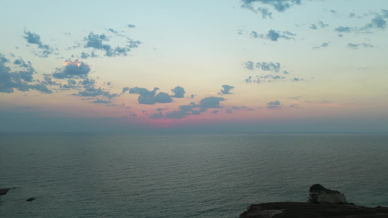 Cielo serale dai tenui colori pastello con nuvole sparse che risplende sopra un mare calmo e aperto
