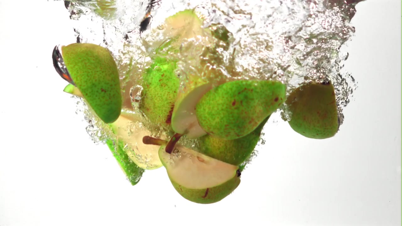 Fette di pera verde fresca che cadono nell'acqua al rallentatore