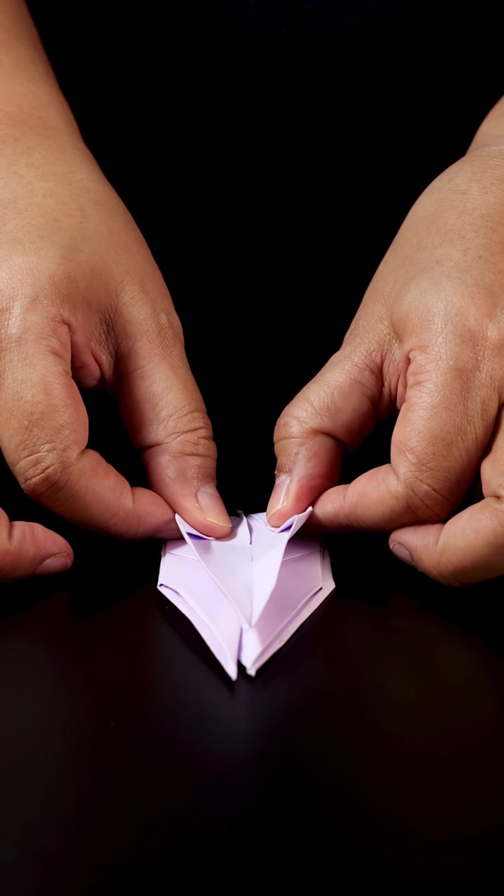 Mani adulte piegano con cura carta rosa per creare un uccello origami, vista dall'alto, illuminazione da studio, primo piano.