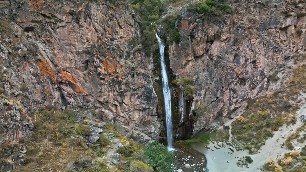 Picturesque waterfall flows down rocky cliff in wild Kyrgyzstan valley