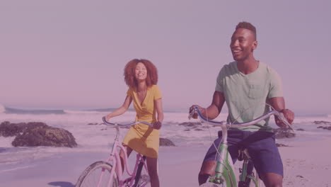 puntos de luz contra una pareja afroamericana montando bicicletas juntos en la playa