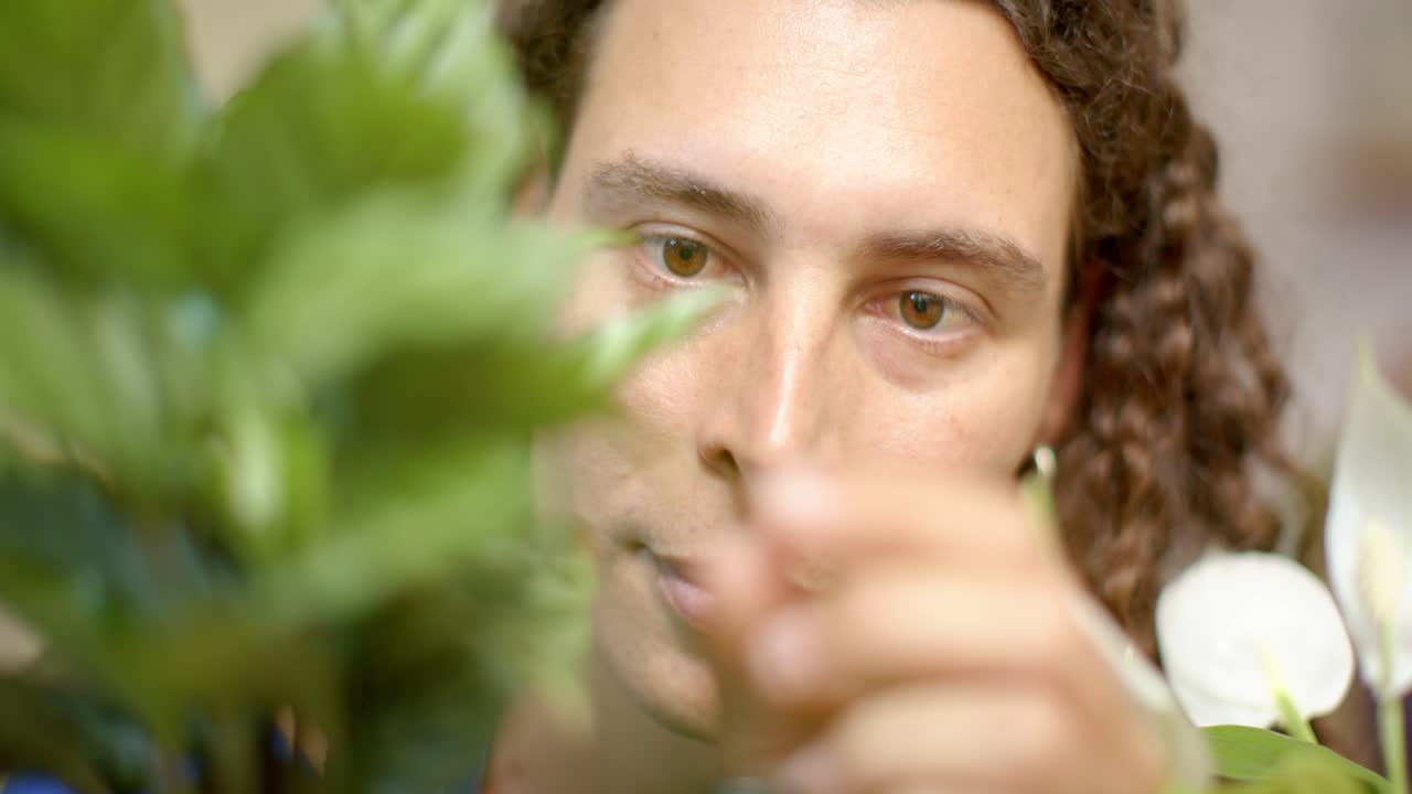 En ikke-binær afroamerikansk voksen person oppdager et blad, klyper forsiktig stilken og steller orkideer hjemme.