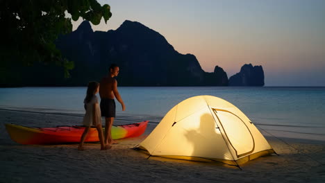 father and daughter camping on a tropical beach at sunset with kayaks