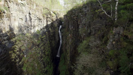 un avión no tripulado volando hacia una gran cascada dentro del estrecho y rocoso desfiladero de corrieshalloch en las tierras altas escocesas