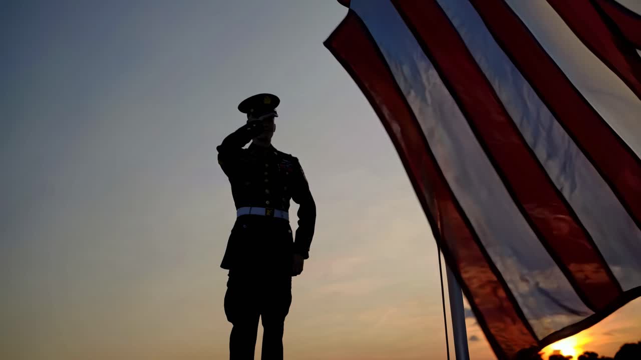 Silhouette of a soldier saluting a flag at sunset, captured from a low angle