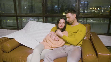 front view of a couple hugging and talking sitting on sofa in the living room at home