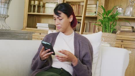Sad-biracial-teenager-girl-sitting-on-sofa,-using-smartphone-and-crying,-in-slow-motion