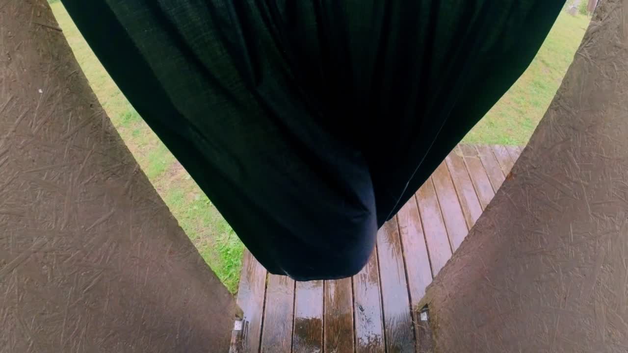 View through parted dark curtain catching wind revealing a rain-soaked wooden deck floor framed by brown curved walls. Shot in the Baltics
