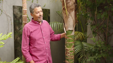 man in garden, standing next to tree, wearing pink shirt, looking thoughtful, copy space