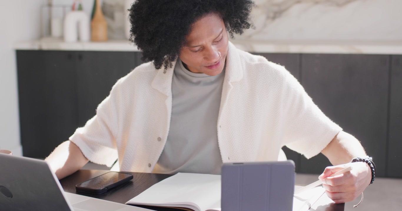 African American man checking tablet, annotating papers with pen, typing on laptop for work at home