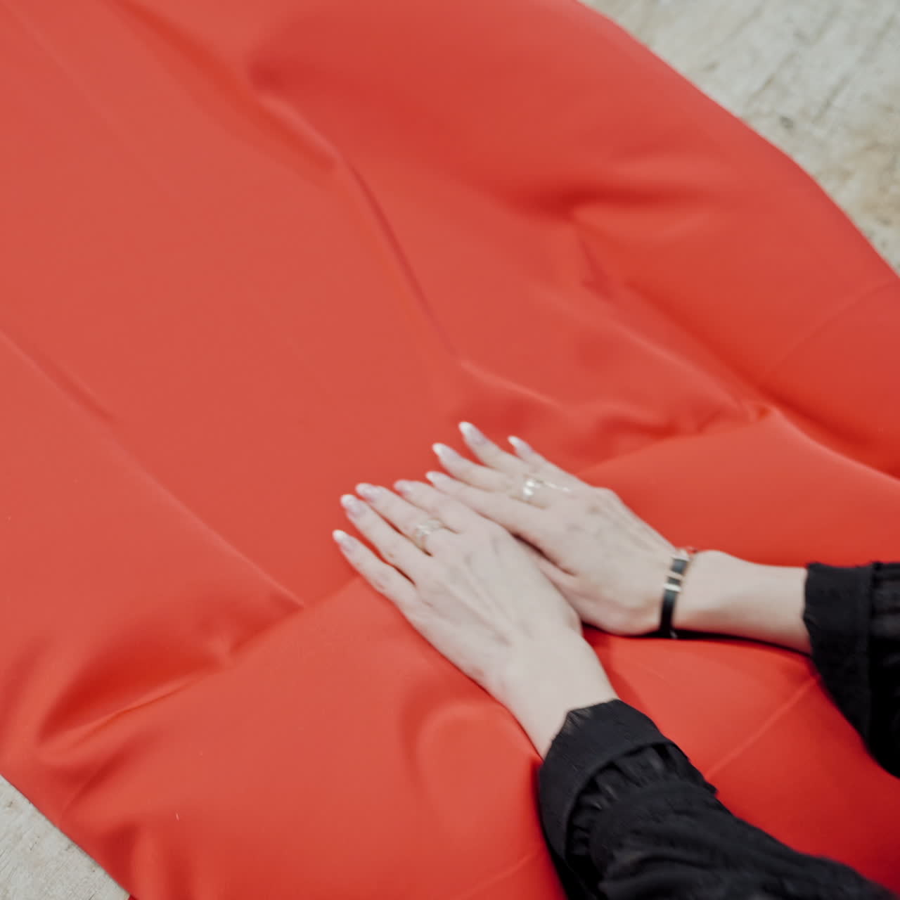 Femile tailor is layng out bright red fabric on the wooden table. Large piece of red material in the hands of a seamstress in workshop.