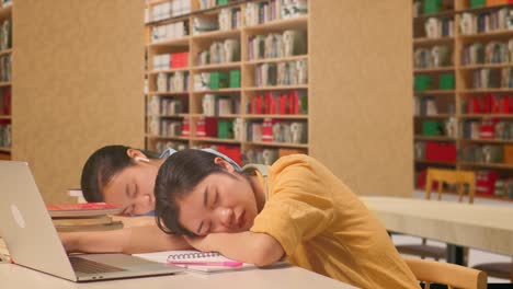 asian woman students with headphones sleeping while sitting and reading books on the table with laptop in the library