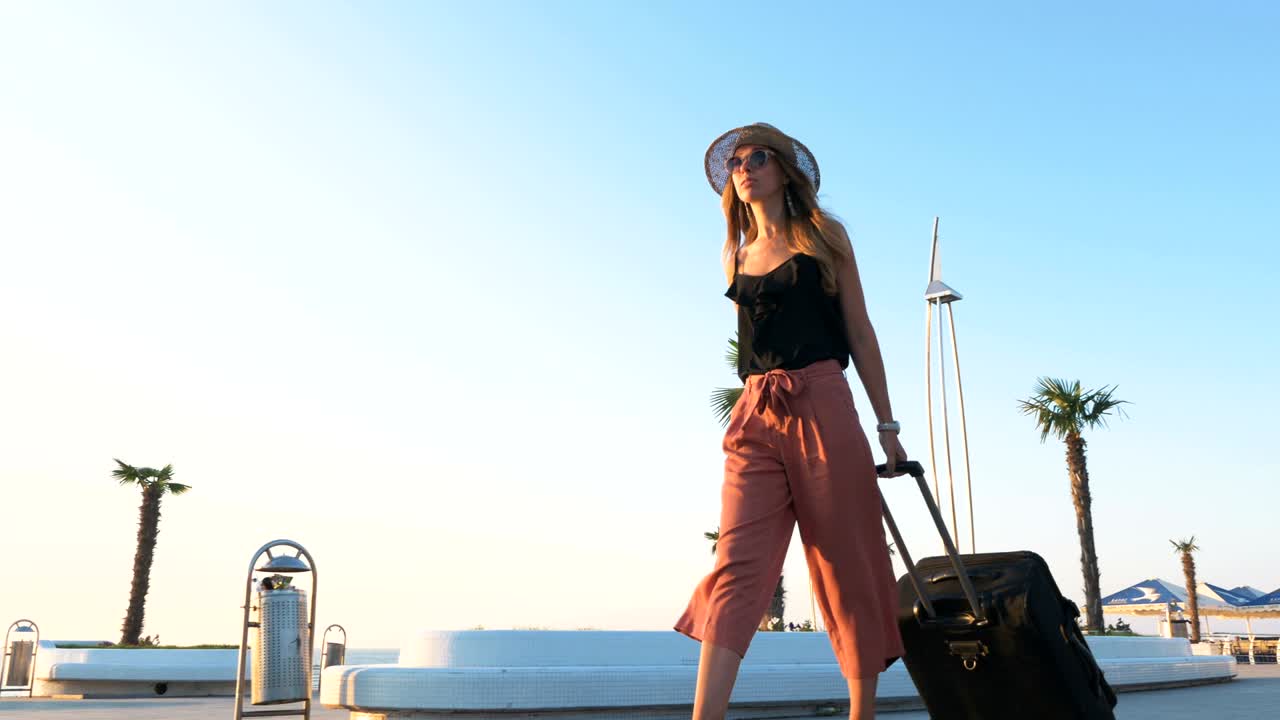 joven mujer de negocios caminando con una maleta en el paseo marítimo durante el atardecer