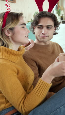 vertical video: couple wearing reindeer antlers enjoying cozy holiday moment with hot drinks