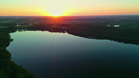 a still lake in a green forest during a golden sunset - pullback aerial reveal