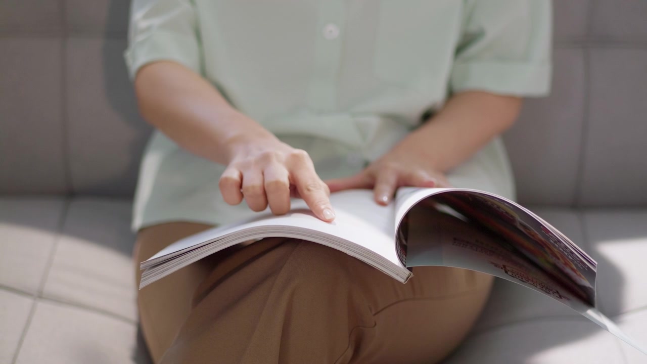Eine Person blättert in einer Zeitschrift in einer hellen Innenumgebung, die einen Moment der Entspannung und Freizeit einfängt.