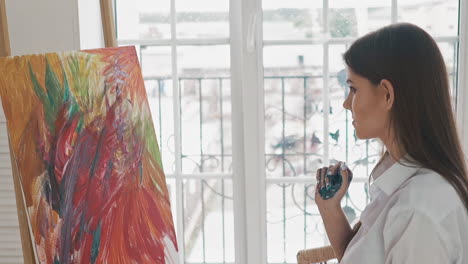 Woman-artist-with-palm-in-paint-looks-at-abstract-painting